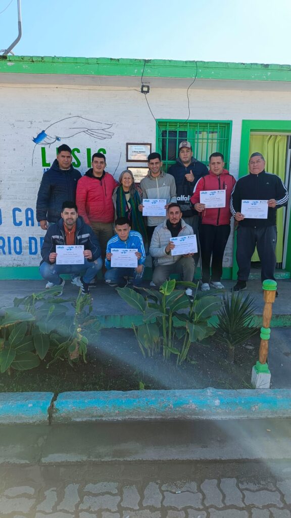 Grupo de personas sosteniendo certificados de alfabetización frente a la fachada de LESIS
