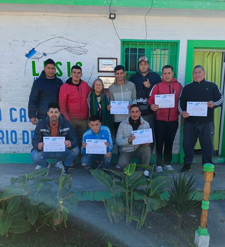 Grupo de personas sosteniendo certificados de alfabetización frente a la fachada de LESIS